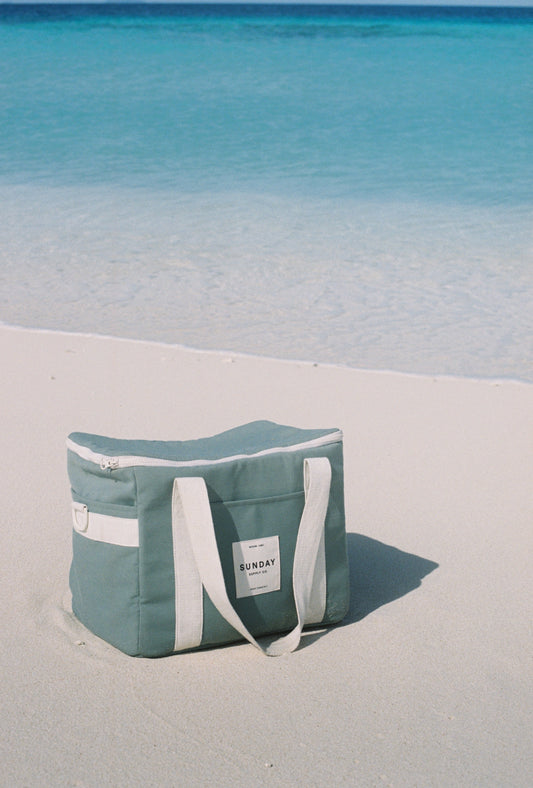 Towelling cooler bag resting on sand beside clear ocean water