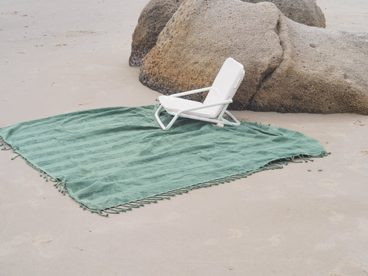Green Tallow beach blanket and white chair set up on the sand for a picnic