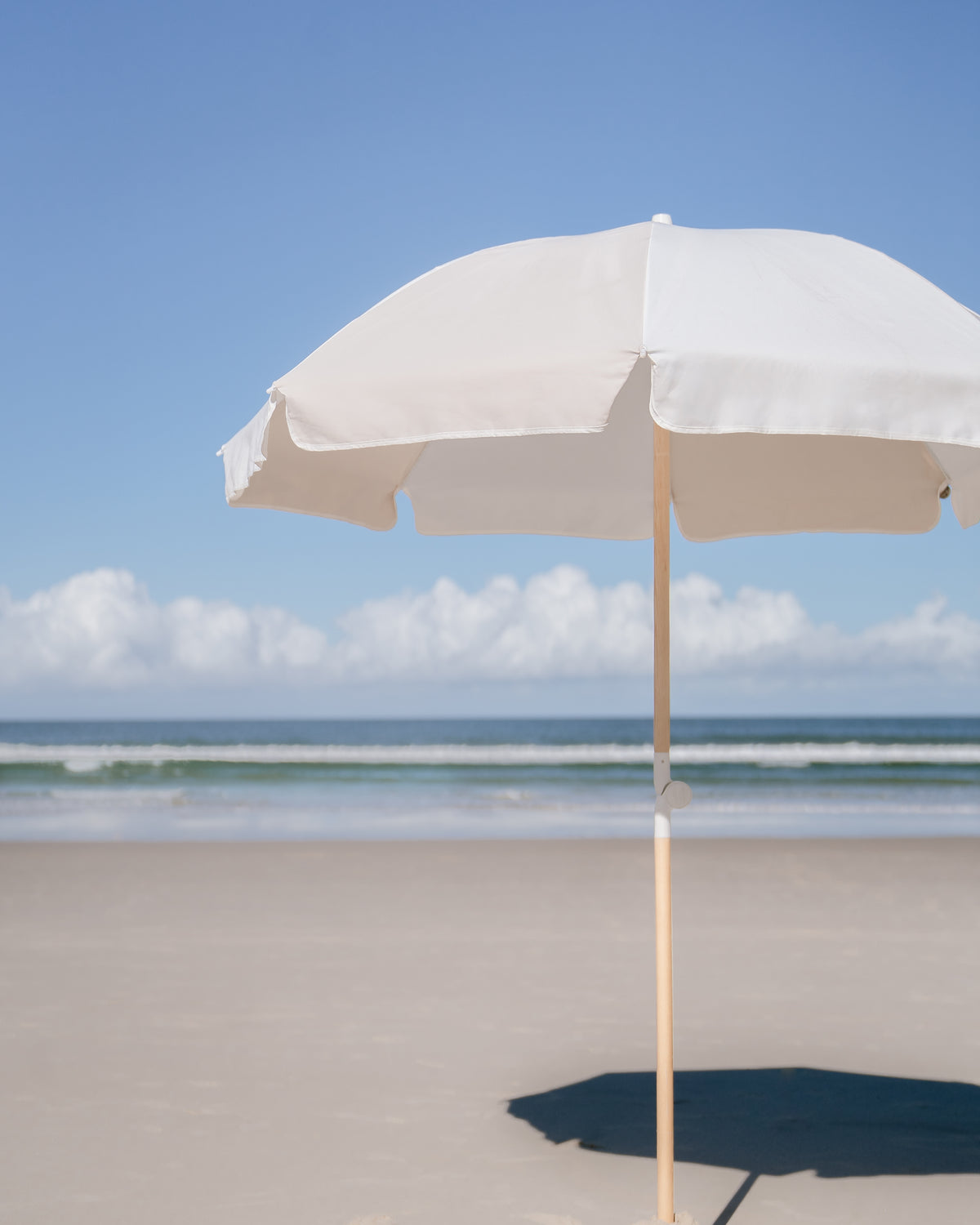 Dunes Splice Beach Umbrella with sand and off-white panels beside the shoreline